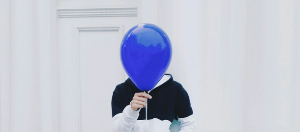 man holding blue balloon in front of his face